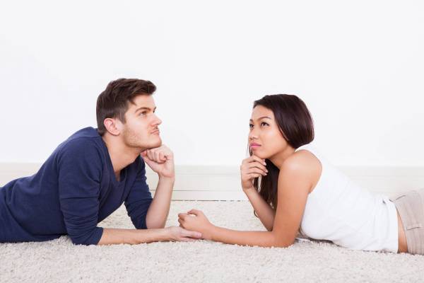 Side view of loving young couple looking at each other while lying on rug at home