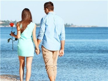 Young couple with red rose walking on beach